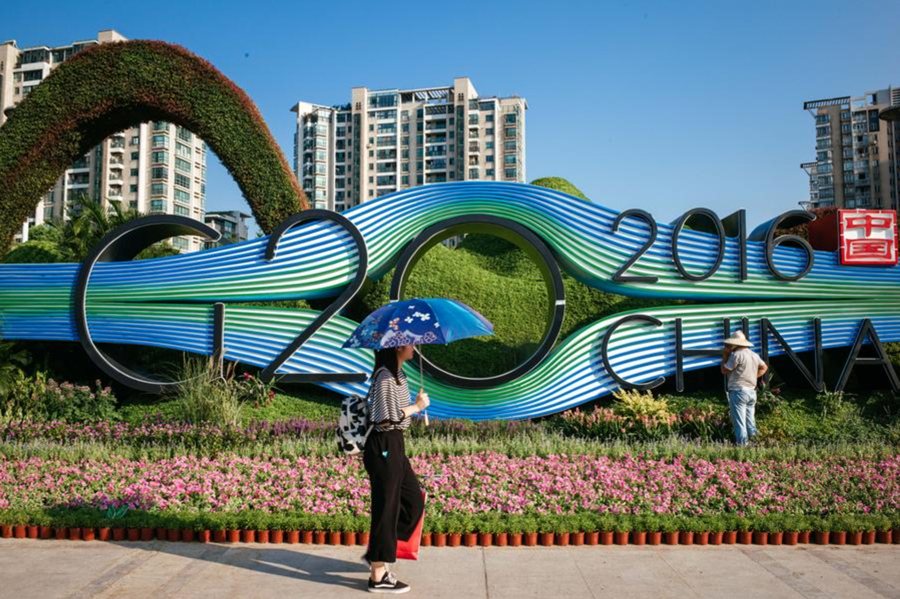 Imagen del 25 de agosto de 2016 de una mujer caminando frente a una cama de flores con la forma del logotipo de la cumbre del G20, en el distrito Binjiang de Hangzhou, capital de la provincia de Zhejiang, en el este de China. (XinhuaZhang Cheng) 